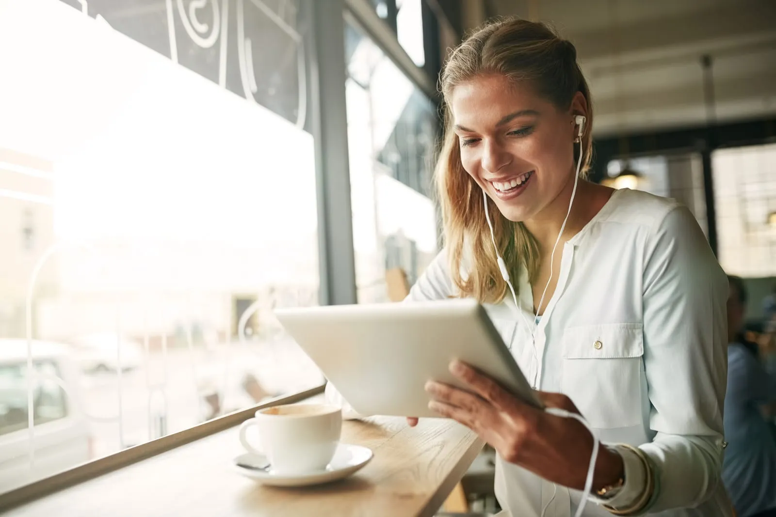 Donna sorridente sfoglia il catalogo corsi da tablet con gli auricolari